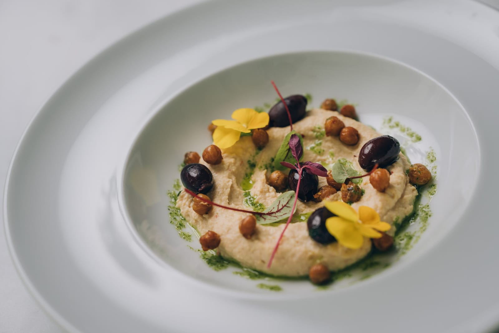 Une assiette de houmous avec pois chiches, olives et fleurs comestibles jaunes