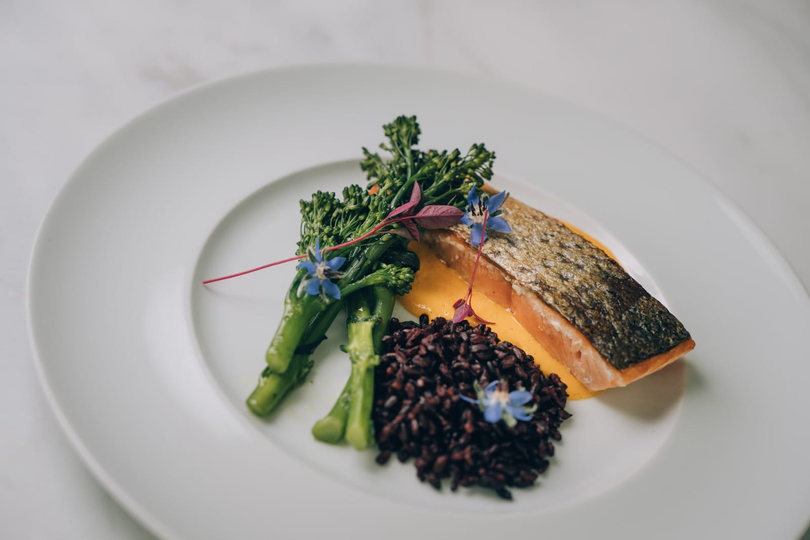 Une assiette de la cuisine de la clinique : saumon rôti, riz noir et brocoli vert, fleurs comestibles