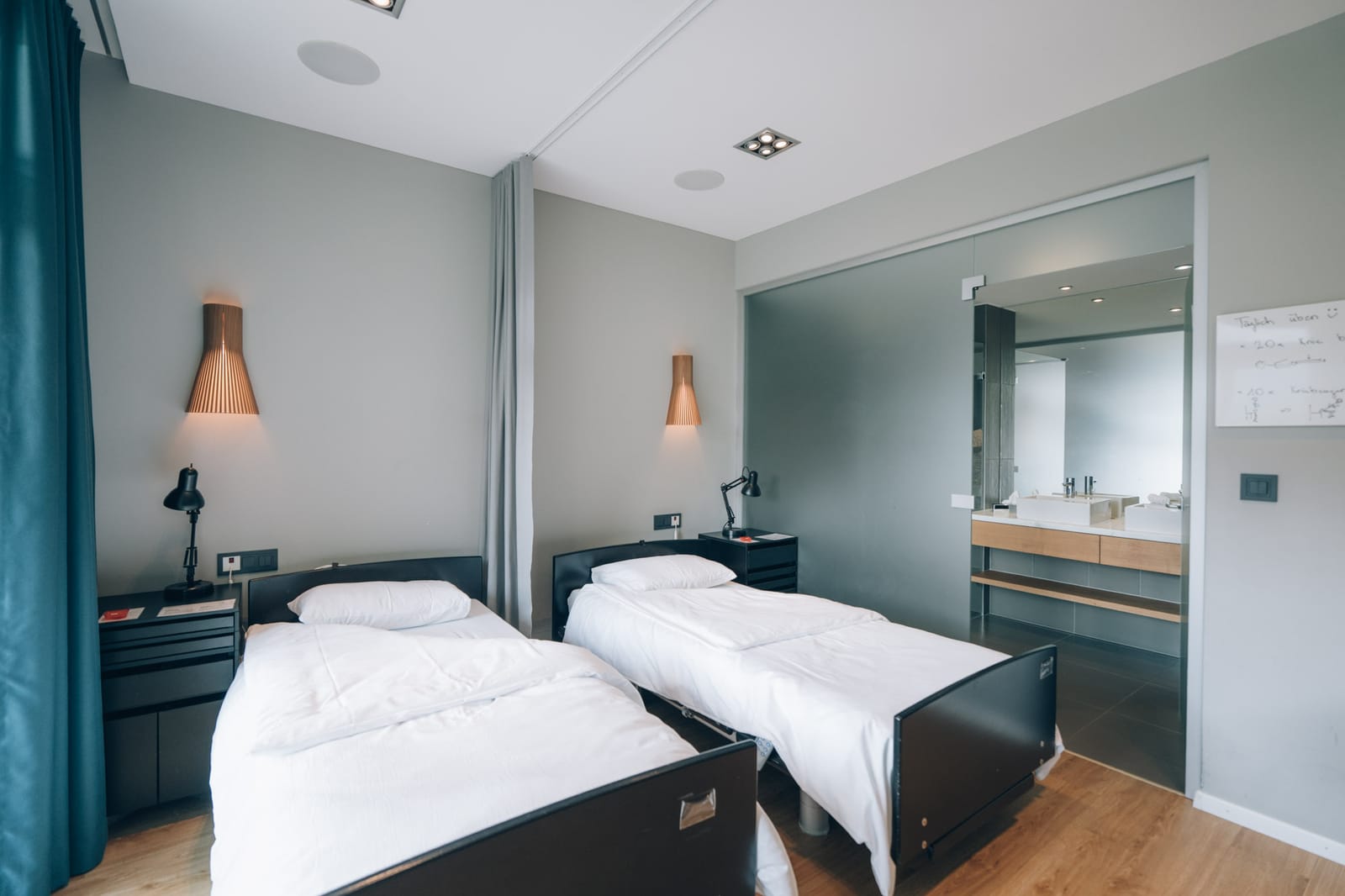 Une chambre à deux lits, appliques en bois, et la vue sur la salle de bain claire