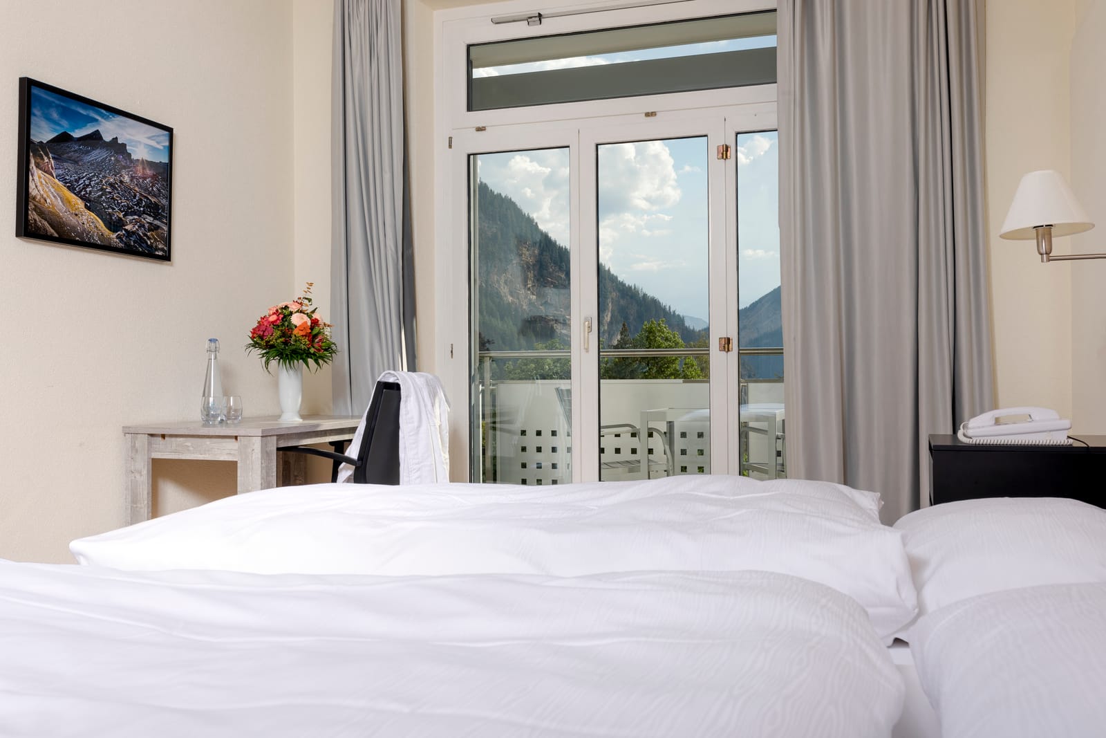 Une chambre double : deux lits, une table et un balcon avec vue sur les montagnes