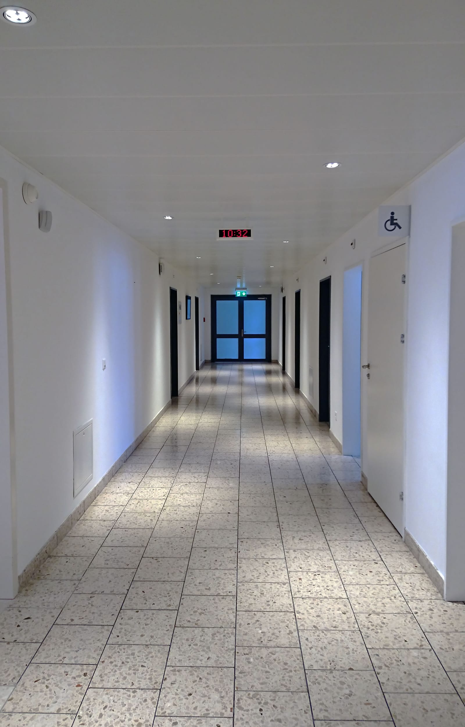 Le couloir du cabinet : murs blancs, portes claires et une fenêtre au bout