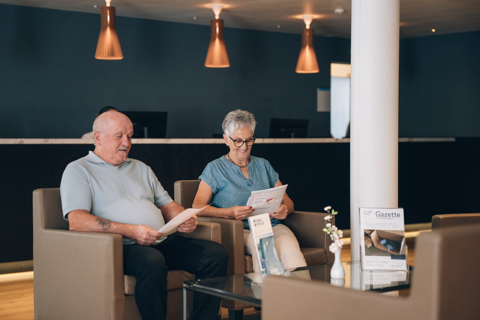 Un couple assis dans les fauteuils du hall d’accueil lit des documents de la clinique