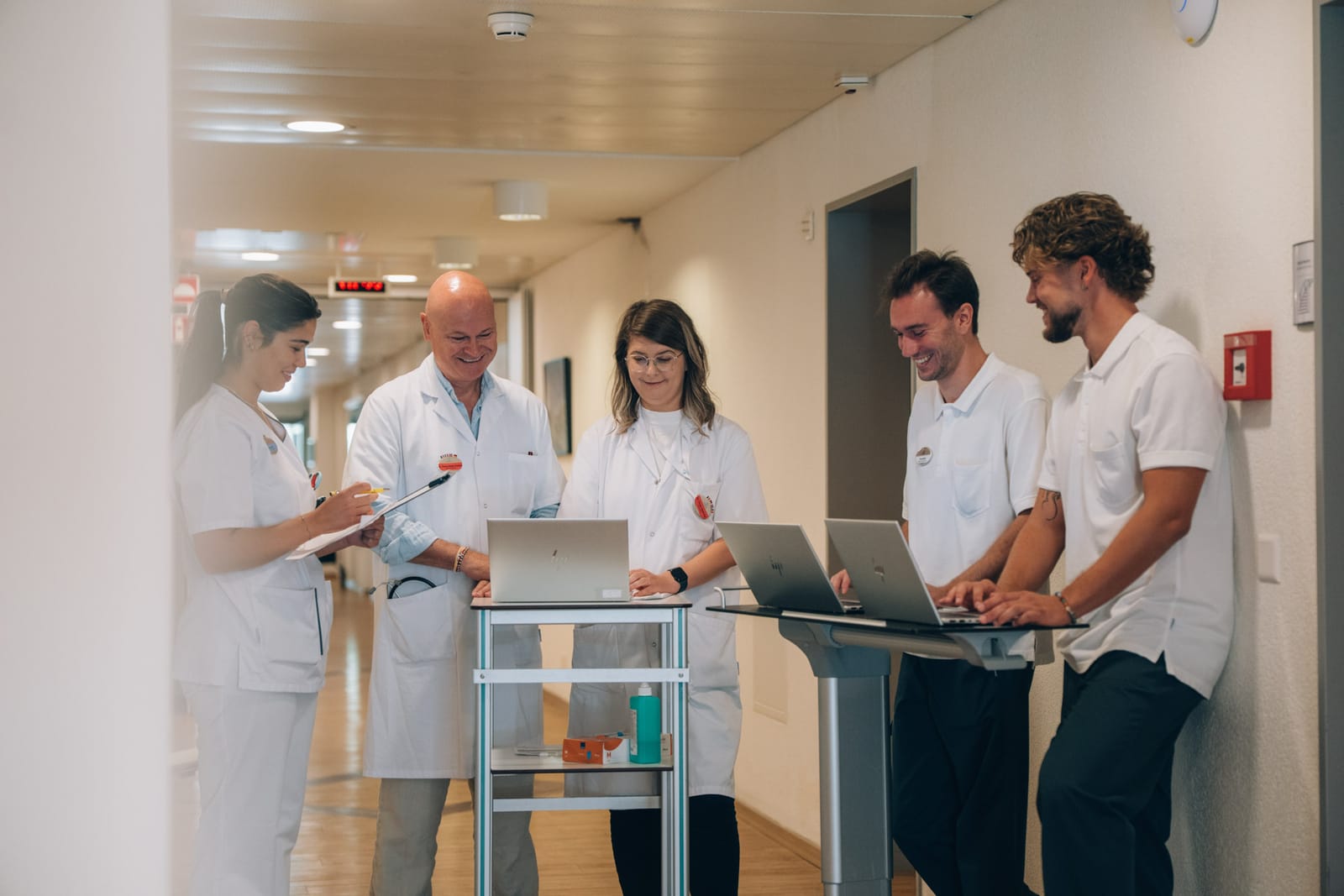 Cinq membres de l’équipe, médecin, soignantes et thérapeutes, se concertent dans le couloir autour de deux chariots de visite et de leurs ordinateurs