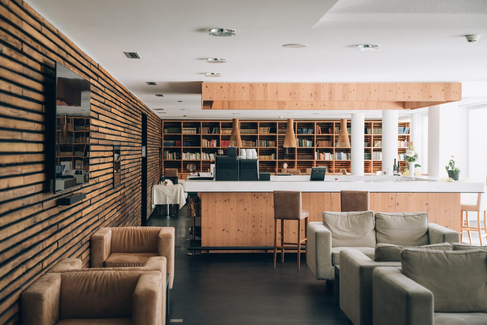 Le salon de la clinique : fauteuils clairs devant une paroi de lattes de bois, puis le bar et le mur de livres