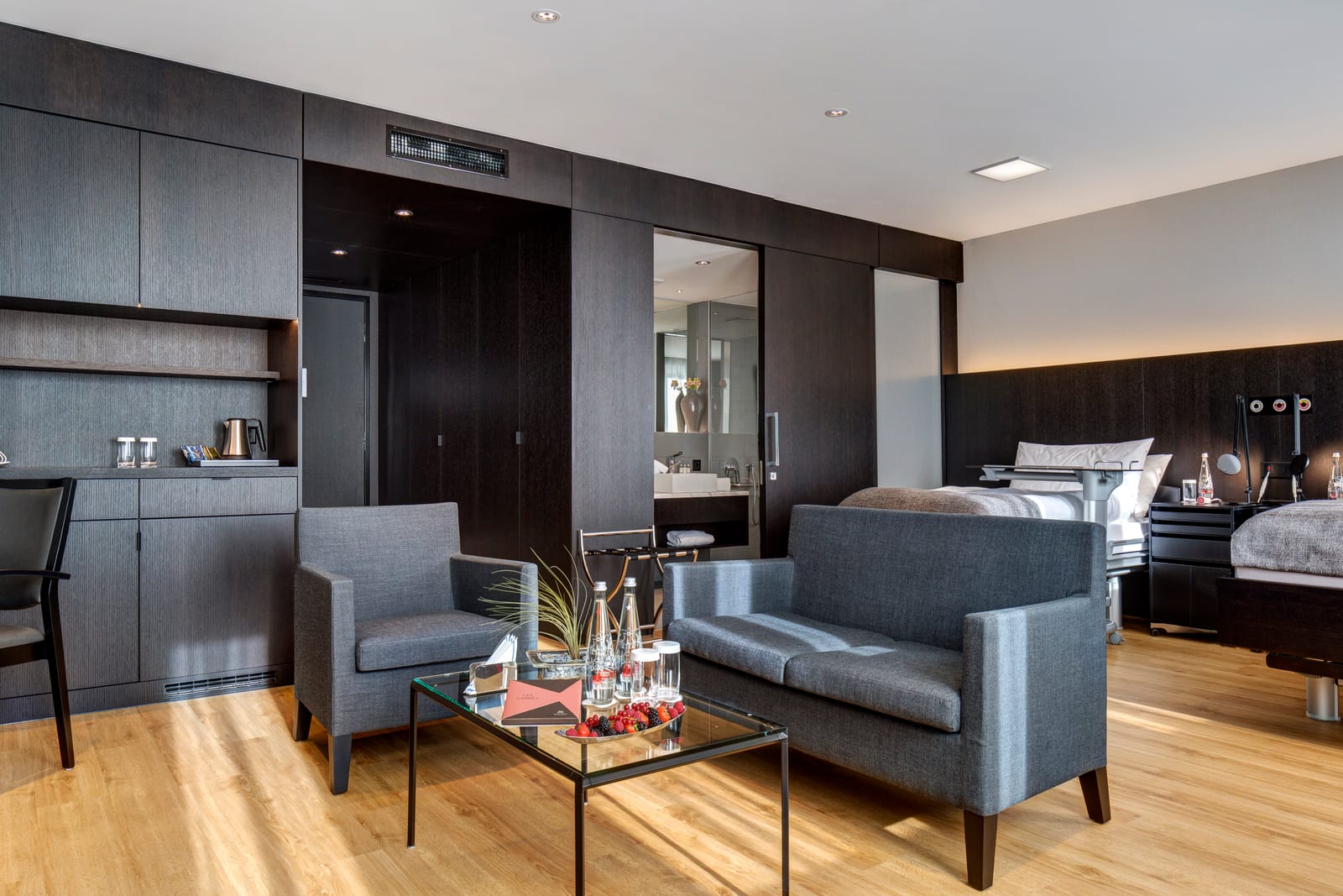 Une junior suite : un coin salon avec canapé, fauteuil et table basse en verre, deux lits au fond