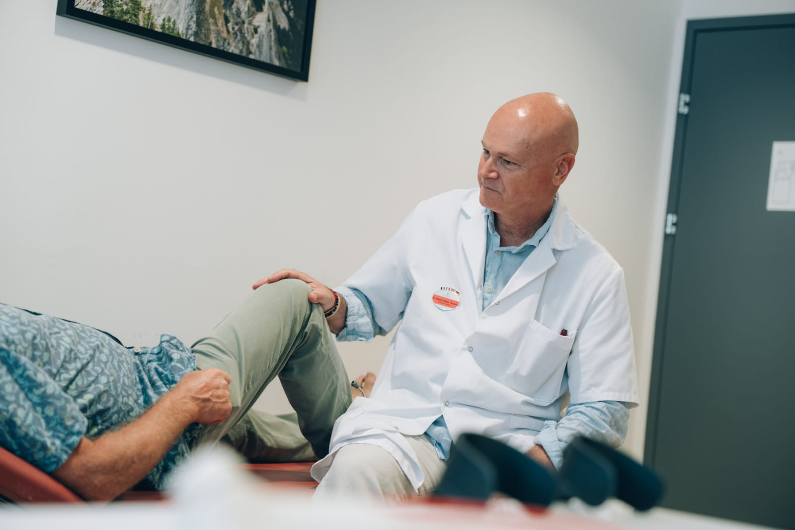 Un médecin assis près de la table d’examen pose la main sur le genou plié d’un patient allongé