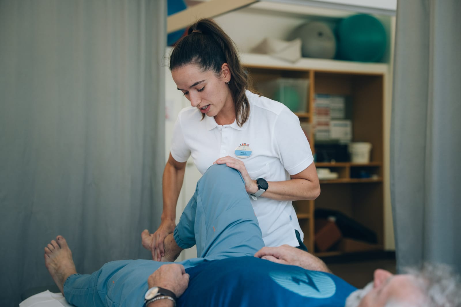 Une thérapeute mobilise le genou plié d’un patient allongé sur la table de traitement