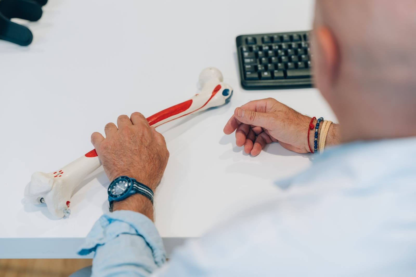 Vu par-dessus l’épaule : les mains d’un médecin tiennent un modèle d’os sur le bureau