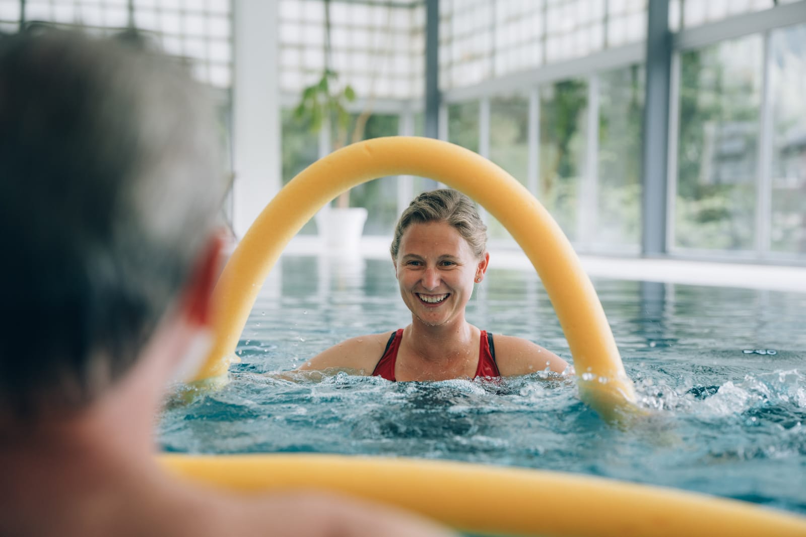 Dans le bassin thermal : une physiothérapeute sourit à un patient qui tient une frite jaune