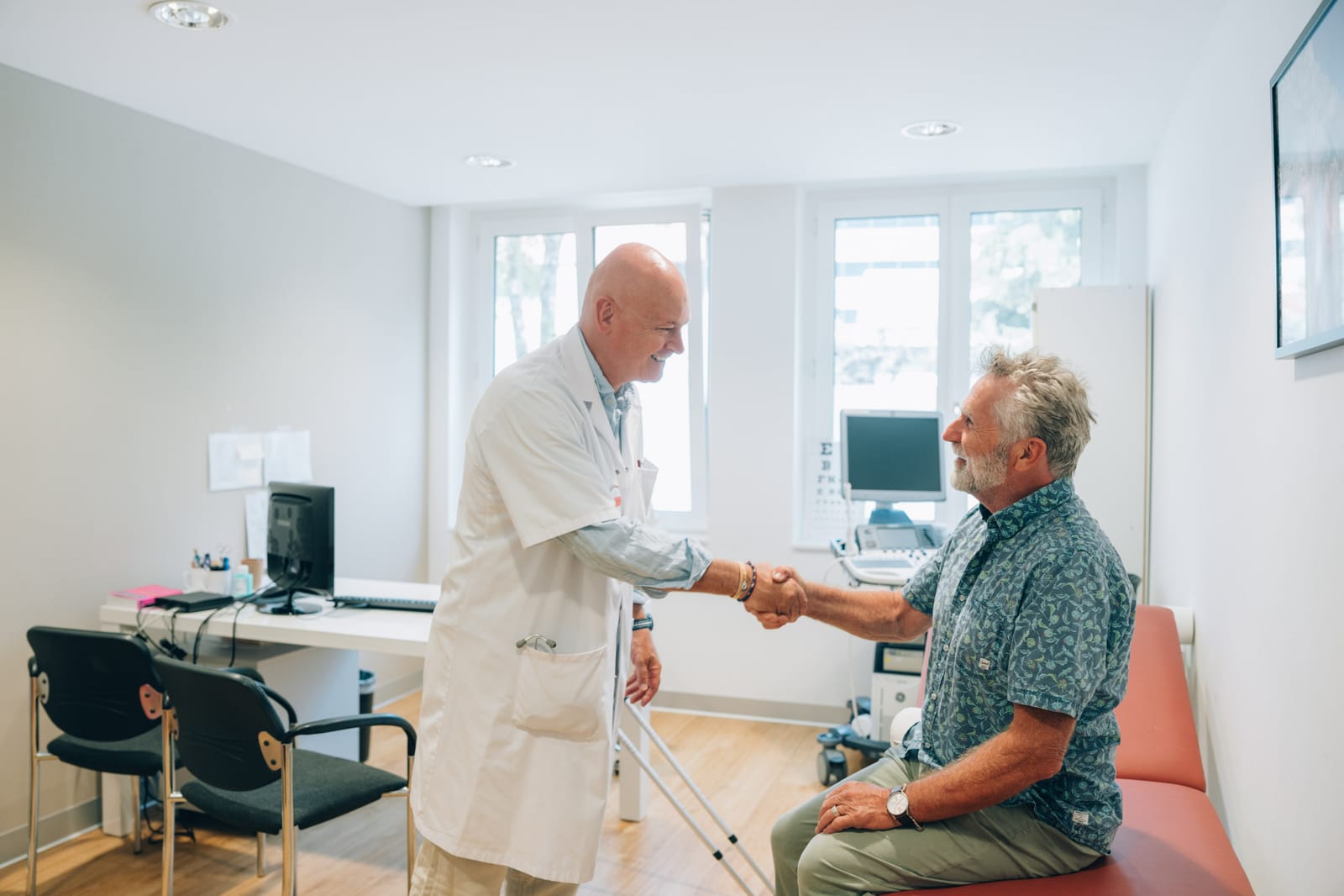 Un médecin serre la main d’un patient assis sur la table d’examen, dans le cabinet de consultation