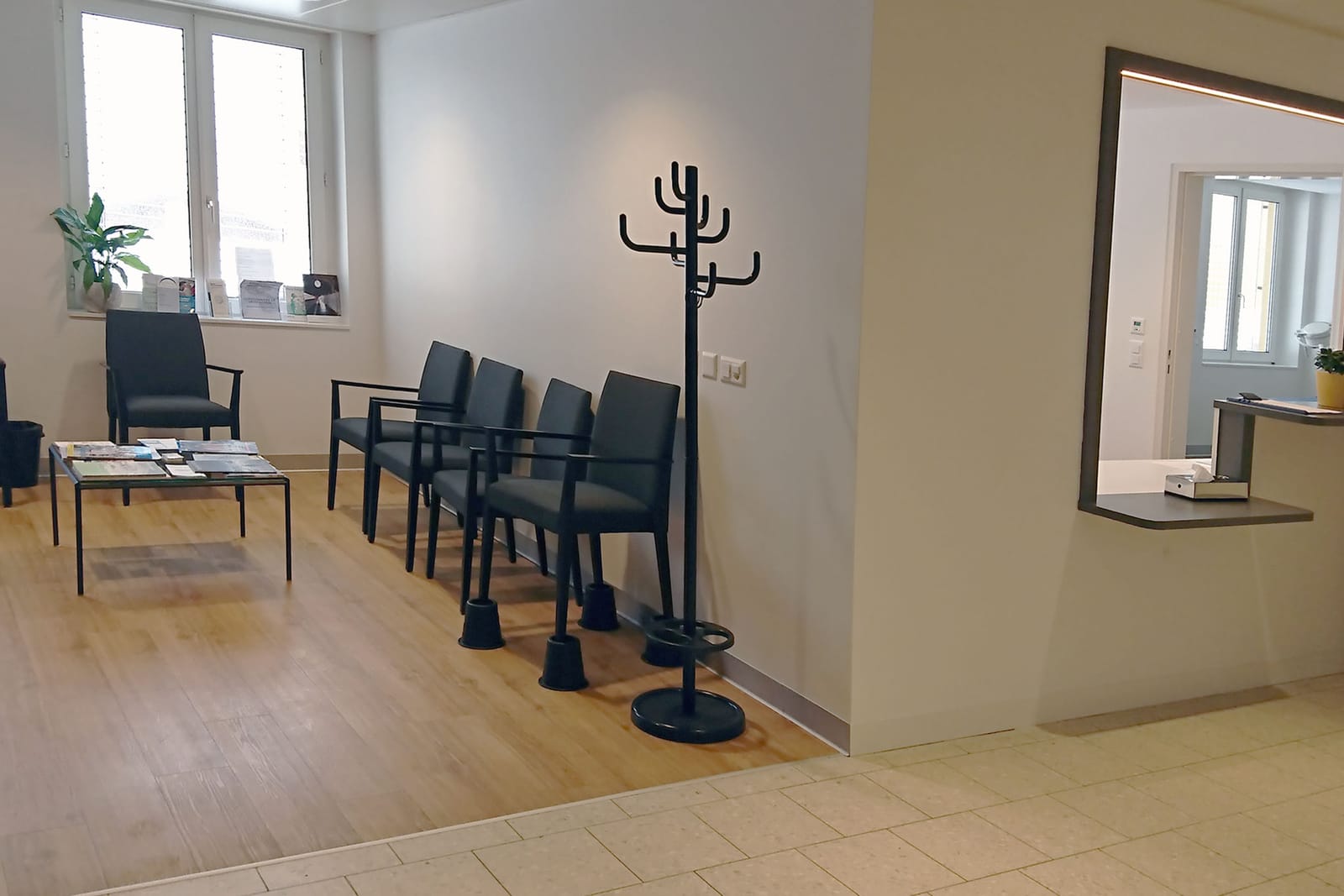 La salle d’attente du cabinet : des chaises le long du mur, une table basse avec des revues, un portemanteau et une fenêtre