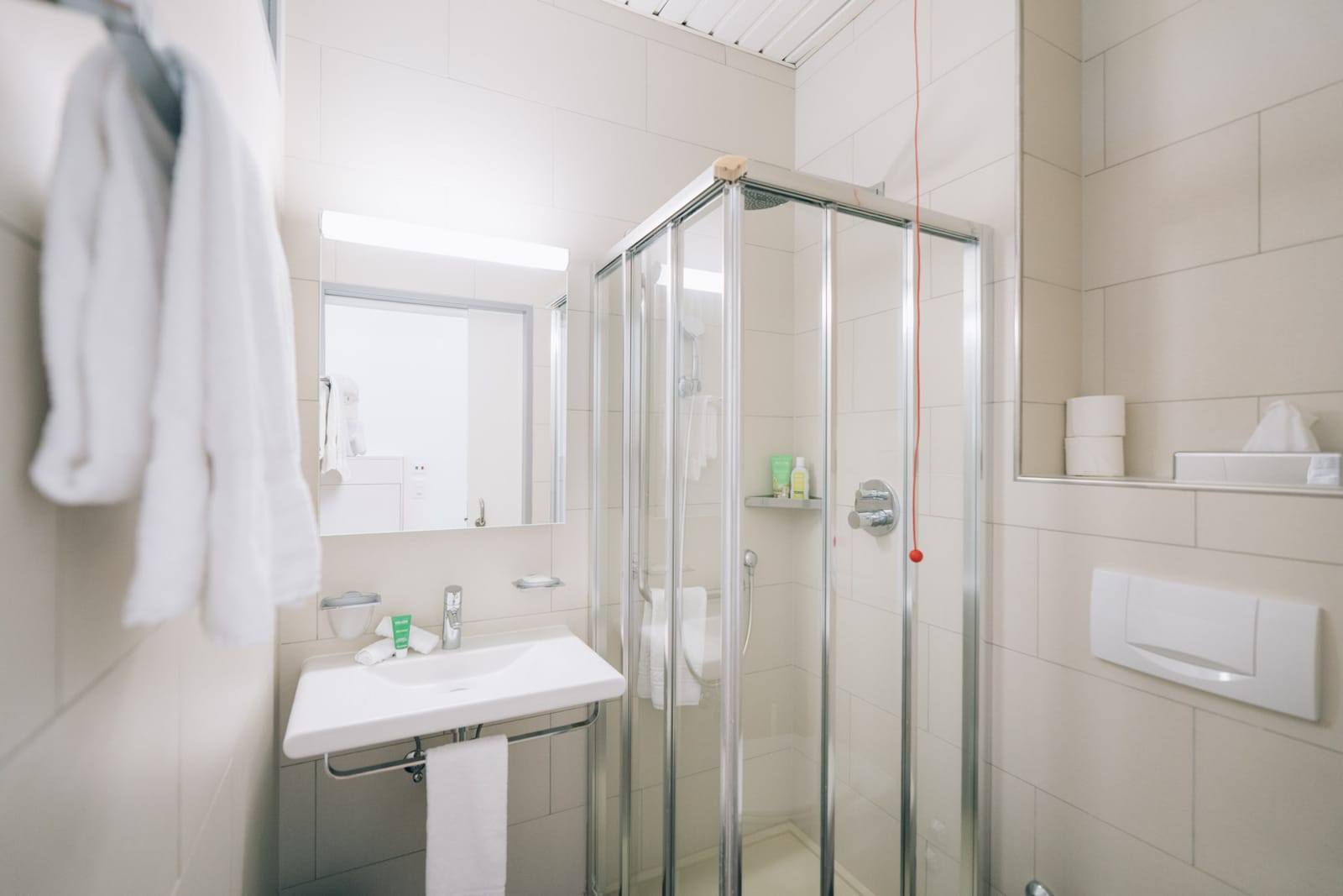 La salle de bain d’une chambre : lavabo, miroir, douche et un peignoir blanc au crochet