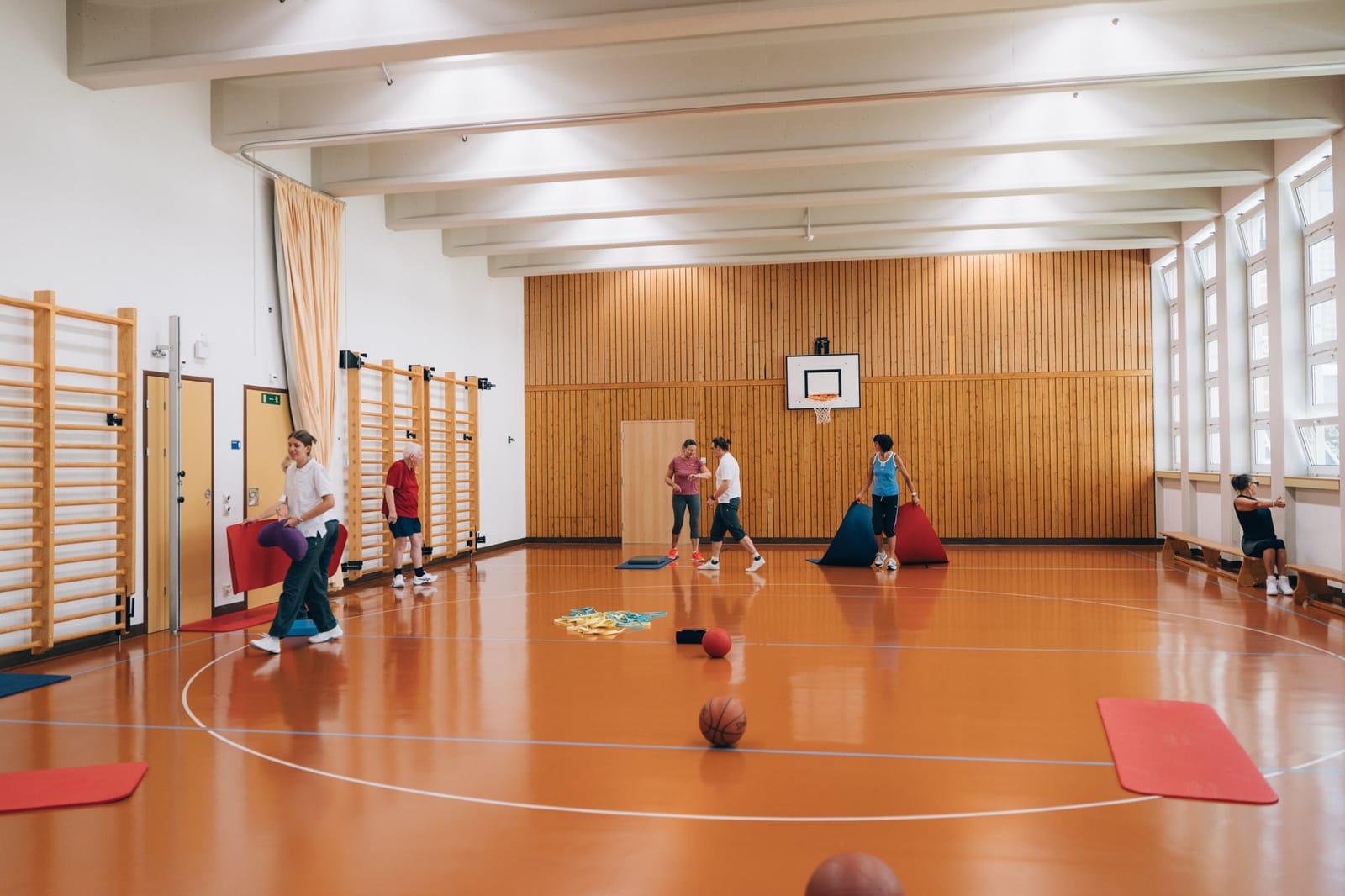 La salle de gymnastique, parquet et espaliers ; à l’autre bout, un petit groupe s’exerce