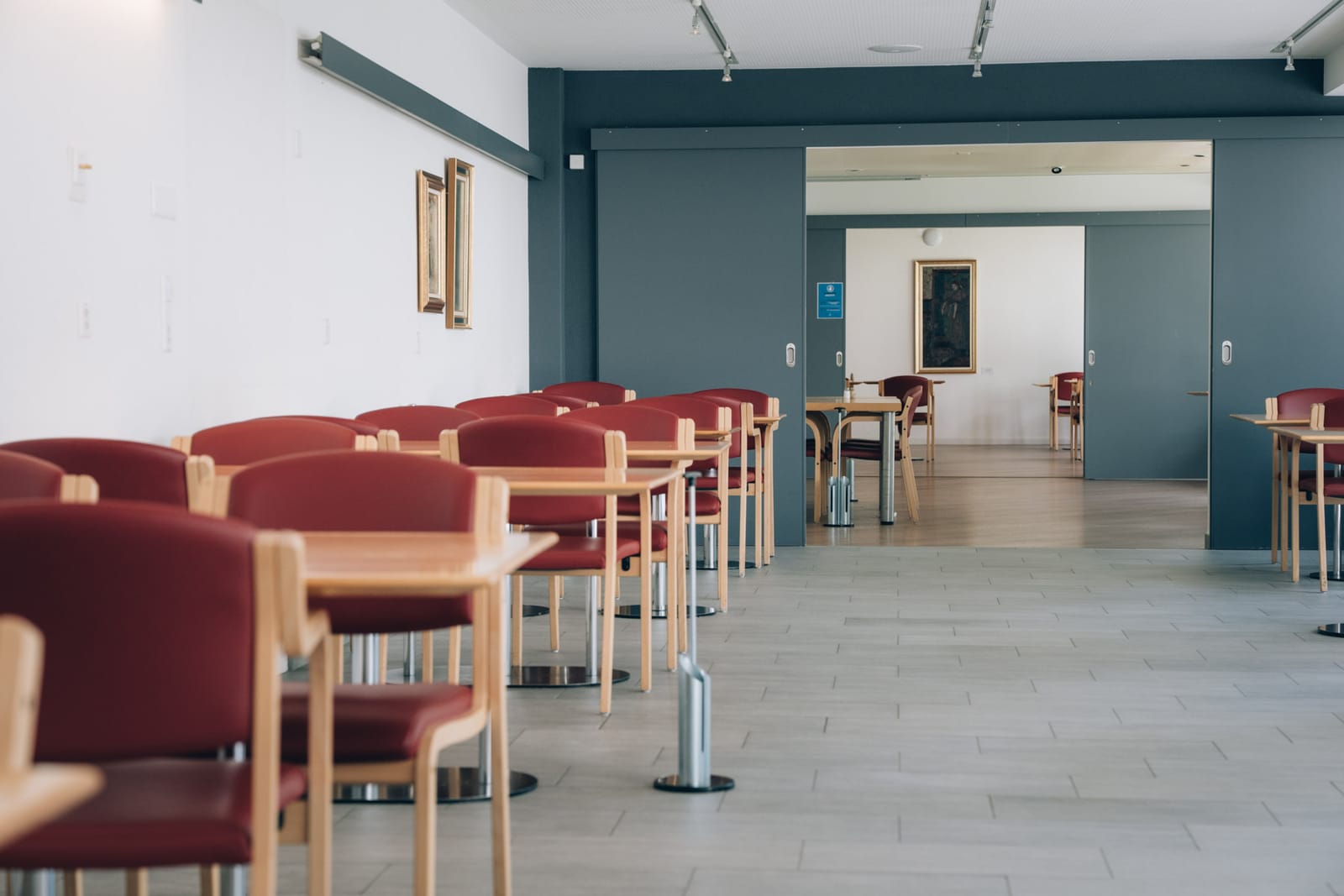 La salle du restaurant : tables en bois clair, chaises rouges, et au fond le passage vers une seconde salle