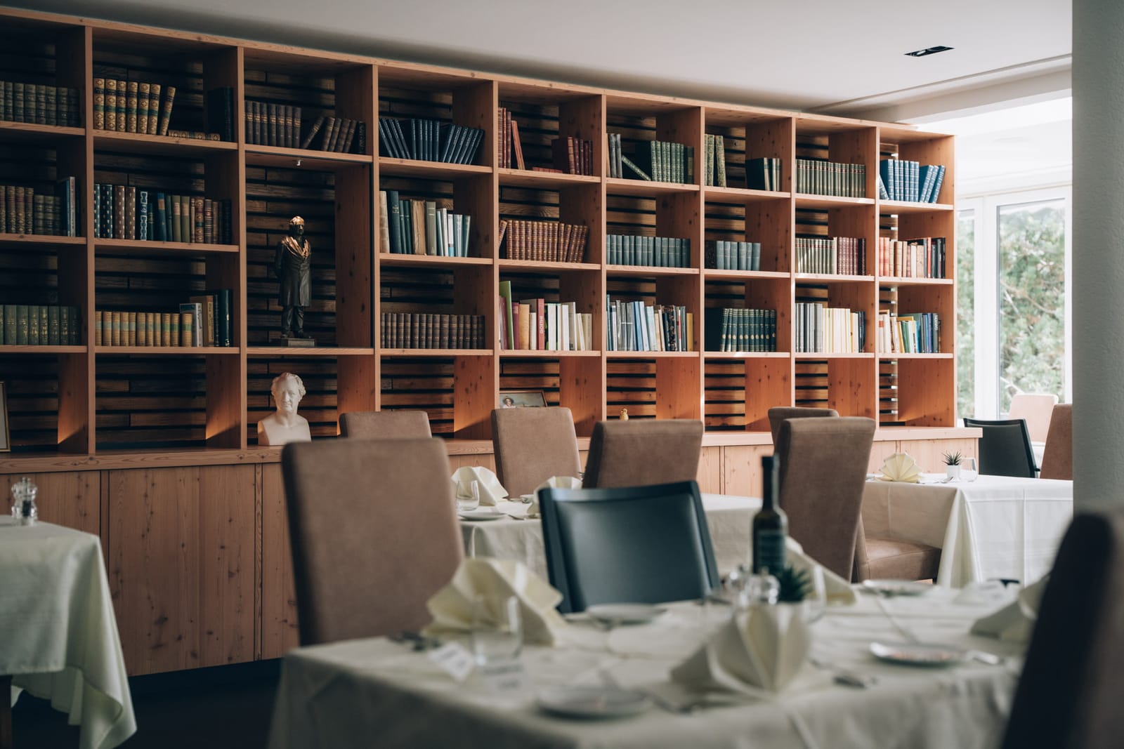 Des tables dressées, nappes blanches, dans le restaurant, devant le grand mur de livres