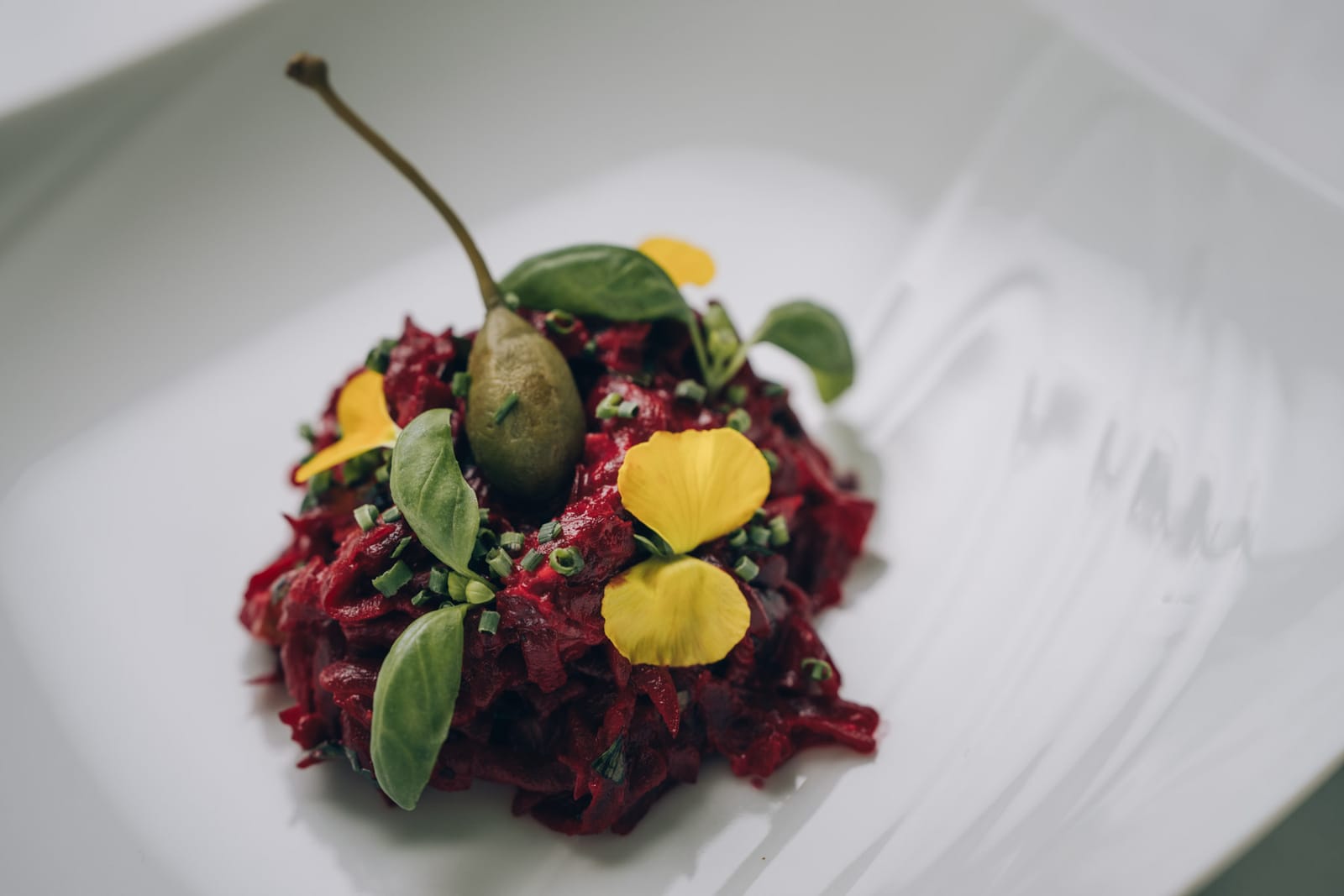 Un tartare de betterave, câpre à queue, herbes et pétales jaunes, sur une assiette blanche