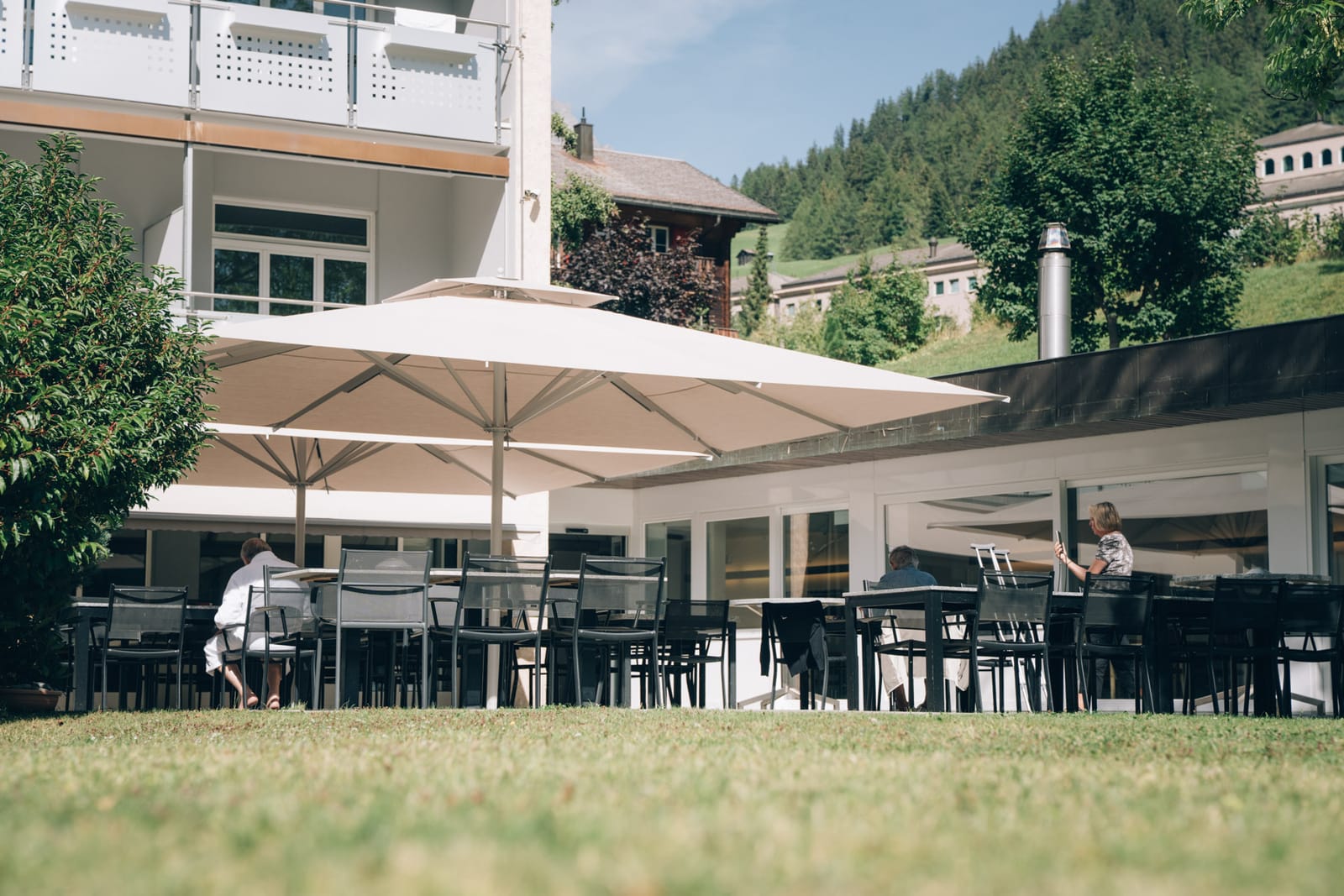 La terrasse de la clinique en été : des tables sous de grands parasols clairs, au bord de la pelouse