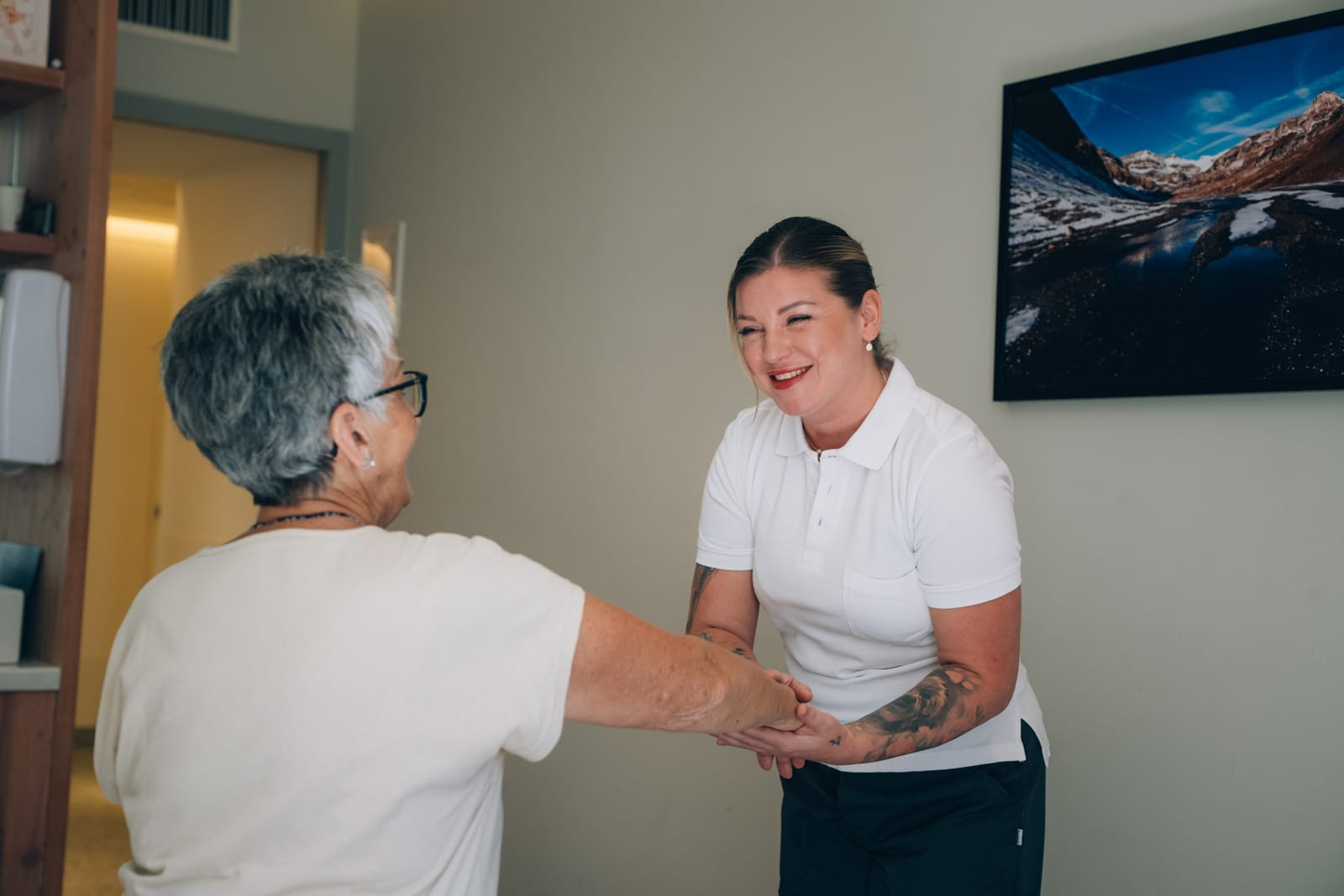 Une thérapeute en polo blanc accueille une patiente en souriant, dans la salle de soins