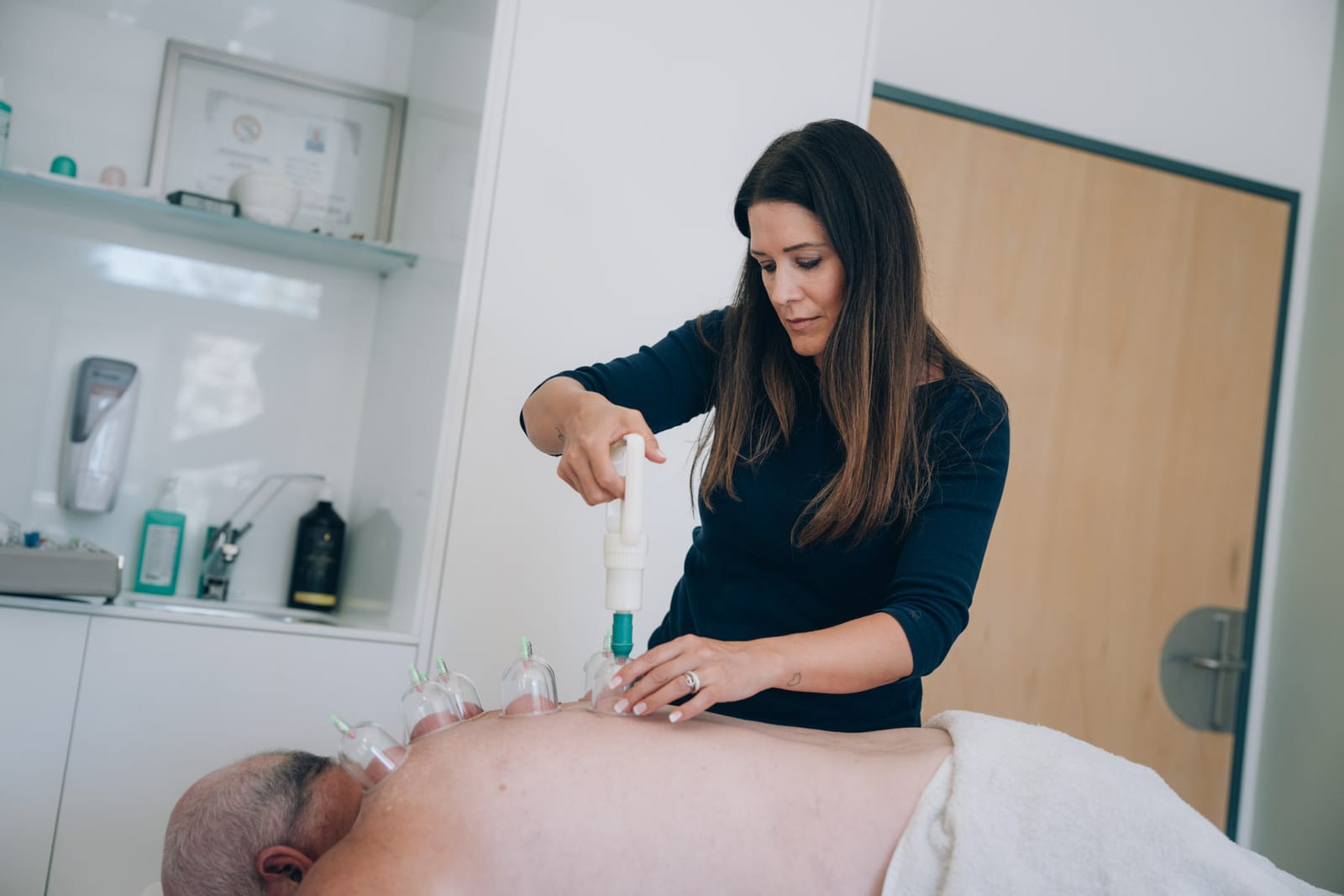 Une thérapeute pose des ventouses avec une petite pompe sur le dos d’un patient allongé sur la table