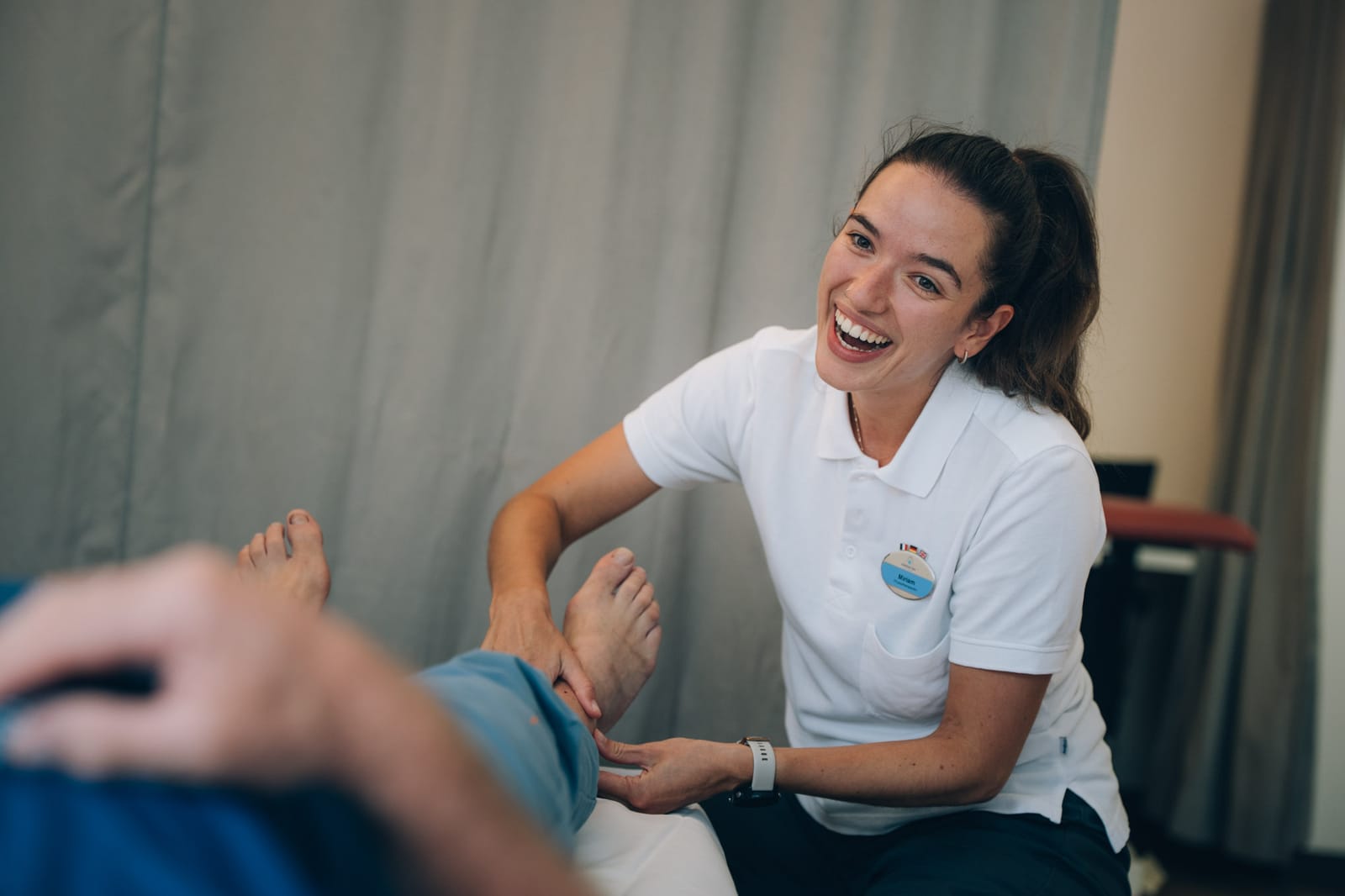 Une physiothérapeute rit en traitant le pied d’un patient allongé