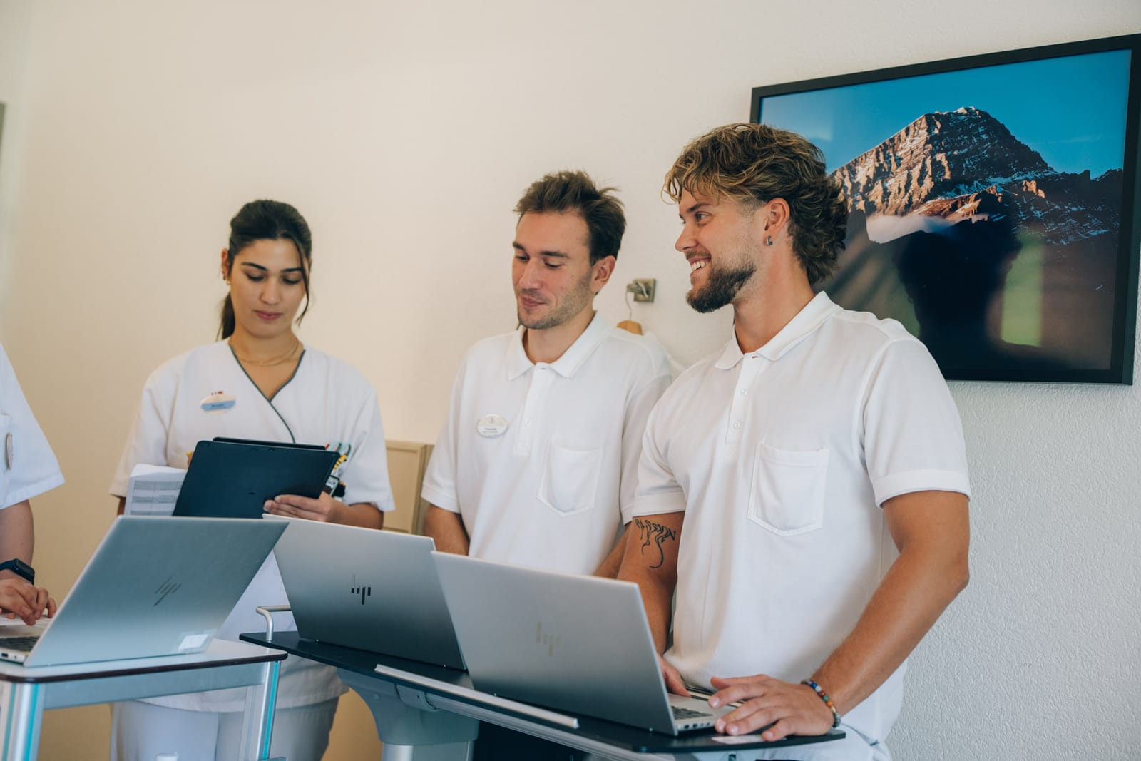 Trois jeunes collègues en tenue blanche travaillent côte à côte sur leurs ordinateurs et une tablette, l’un d’eux sourit