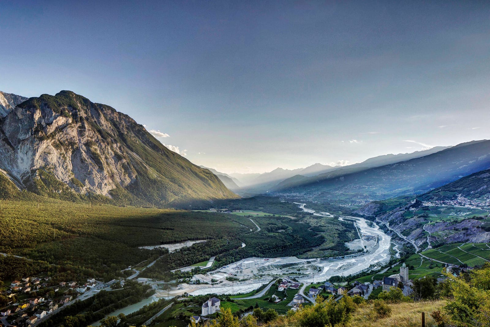 La vallée du Rhône au lever du jour, vue d’en haut : le fleuve, les villages et la route qui monte vers Loèche-les-Bains